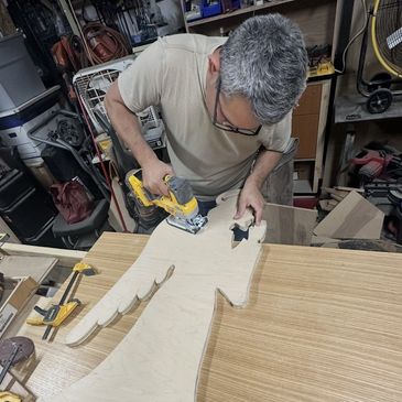 Man using a jigsaw to cut a wooden board in a workshop.