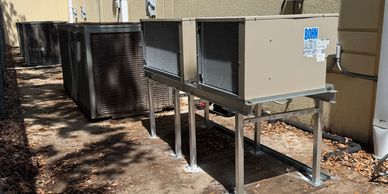 Outdoor HVAC units installed on metal stands beside a building.