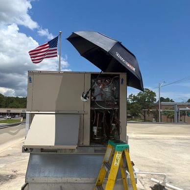 HVAC unit being serviced with an umbrella for shade on a sunny day.