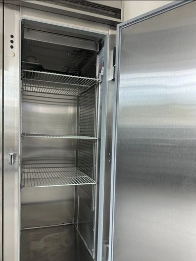Empty stainless steel commercial refrigerator with wire shelves.