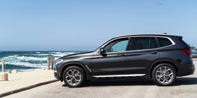 A black SUV parked by the seaside with waves in the background.