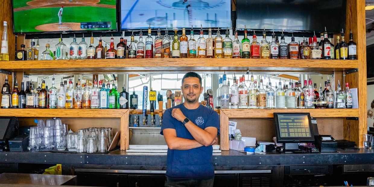 A person standing in a bar with shelves of liquors behind