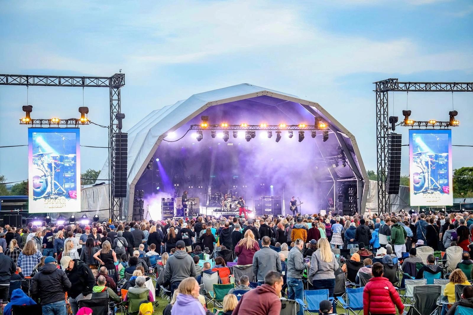 Outdoor concert with large crowd and illuminated stage at dusk.