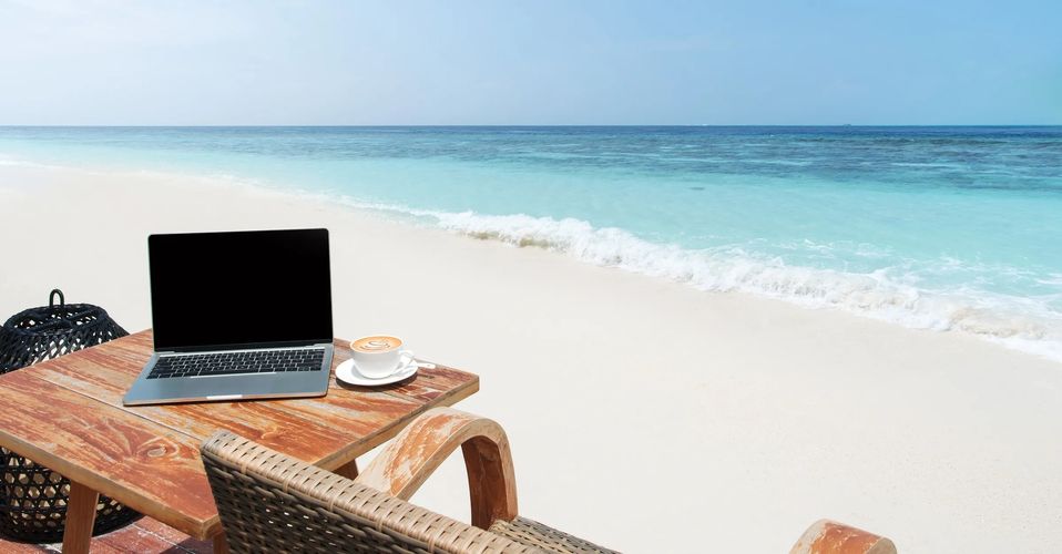 Laptop and coffee on a wooden table by a serene beach.