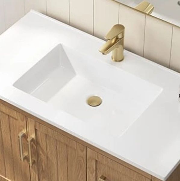 Modern white sink with gold faucet on wooden cabinet.