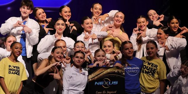 Youth dance team posing together with a Nexus banner on stage.