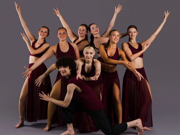 A group of dancers posing in burgundy costumes.