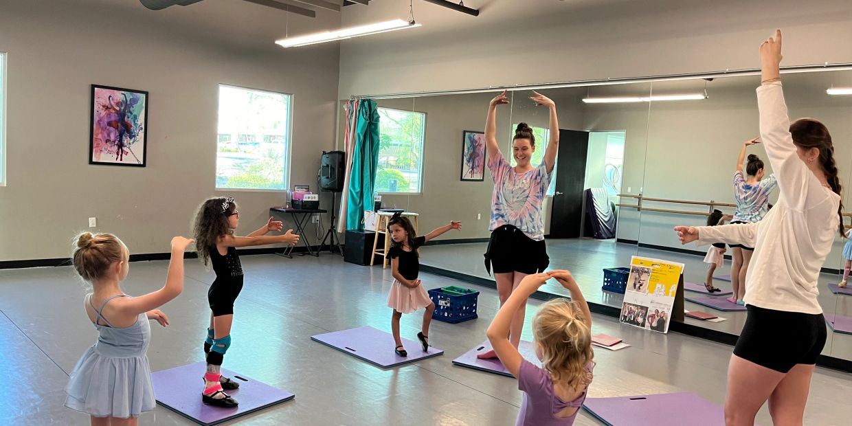 Children practicing ballet with instructors in a dance studio.