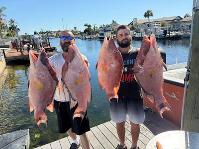 Two men proudly holding large red snapper fish by the dock.