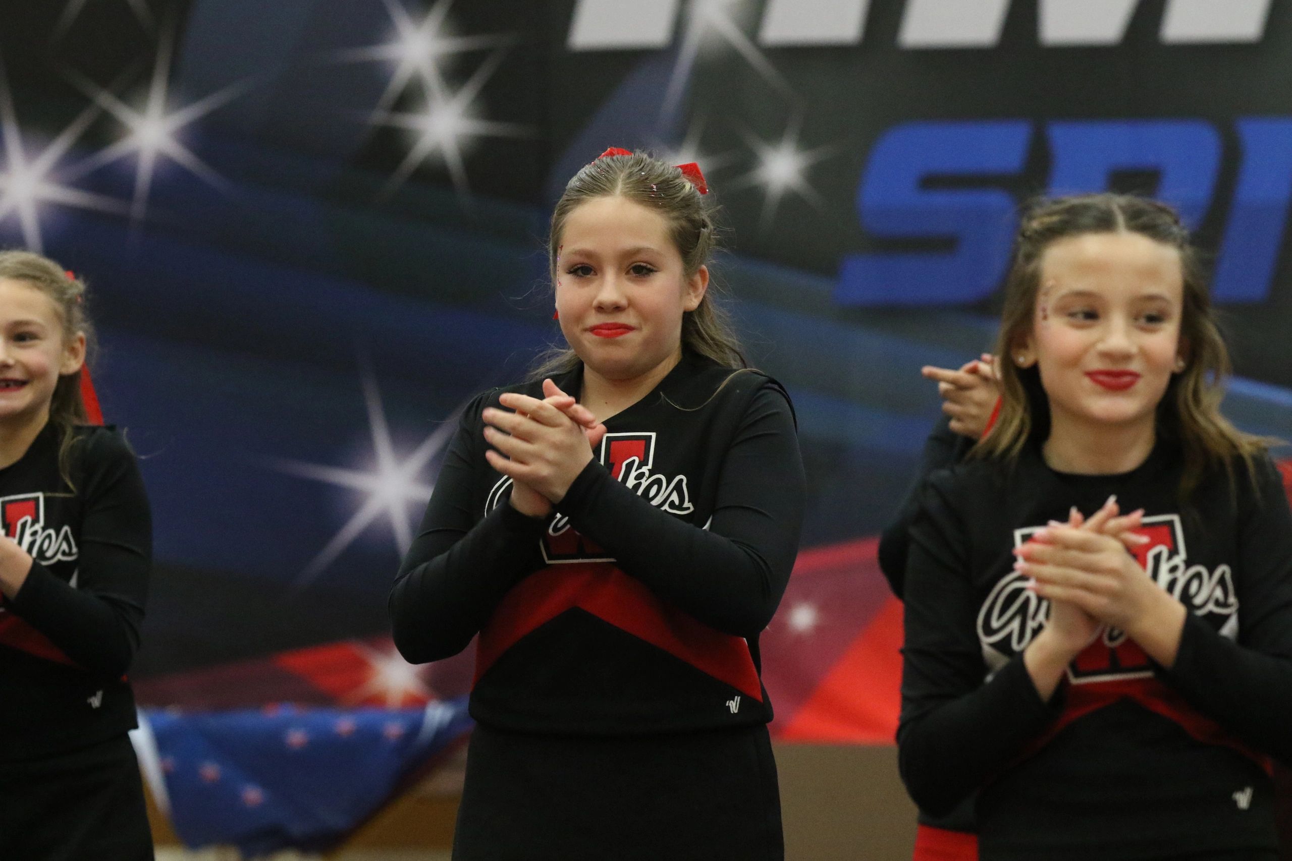 Young cheerleaders in black and red uniforms clapping during a performance.