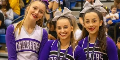 Three cheerleaders in purple Chargers uniforms smiling for a photo.