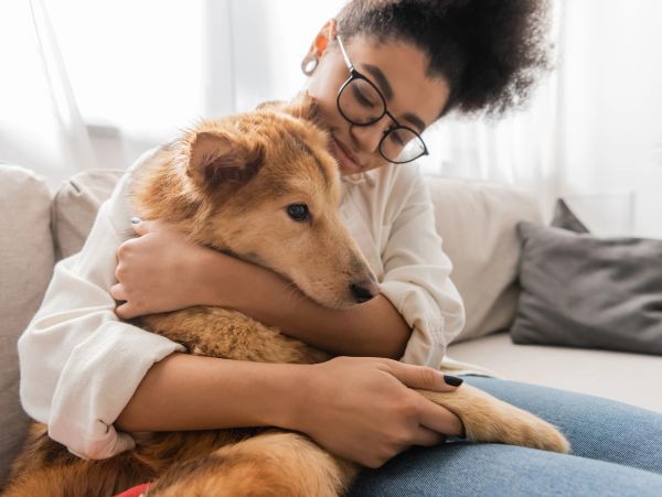 A woman lovingly hugs her golden-brown dog on a sofa.