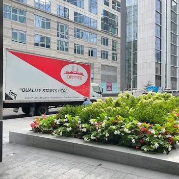 Delivery truck parked near a building with a flower bed in front.
