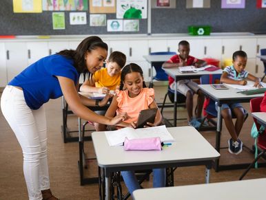 Teacher helping a student with tablet in classroom.