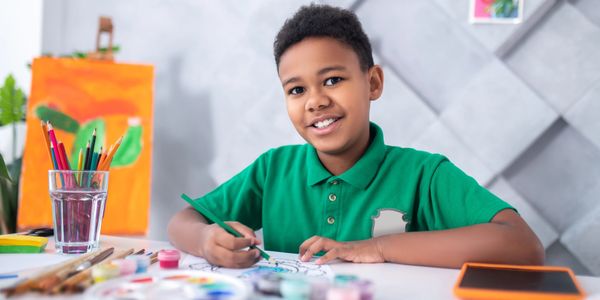 Boy in green shirt painting and smiling.