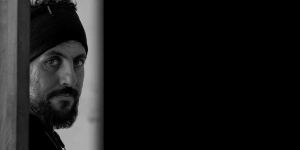 Man with beard and headband looking over a wall.