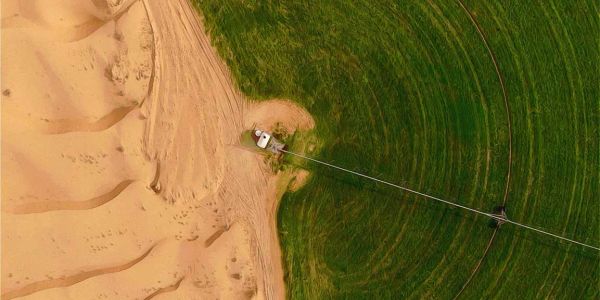Aerial view of irrigation system between sand and green field.