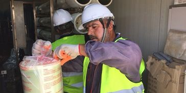 Worker in safety gear handling packaged materials indoors.
