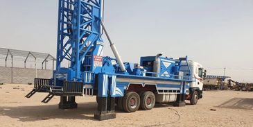 Blue drilling rig mounted on a truck in a sandy area.