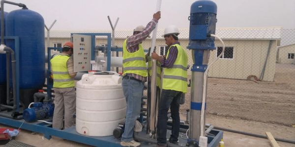 Three workers in safety vests operating industrial water treatment equipment outdoors.