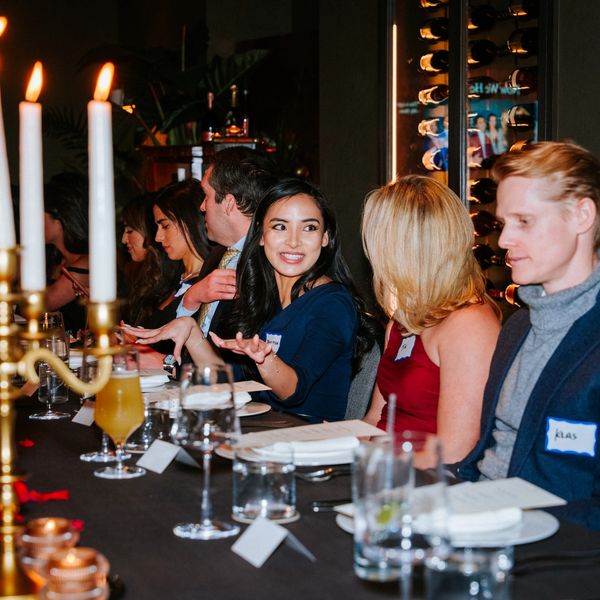 People engaged in conversation at a formal dinner event with candles and name tags.