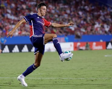 Soccer player controlling the ball mid-air during a match in a crowded stadium.