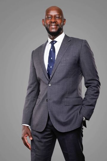 Man in gray suit with blue tie smiling.