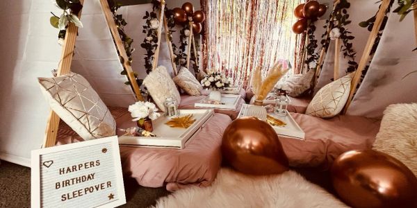 Cozy sleepover setup with pillows, balloons, and personalized sign.