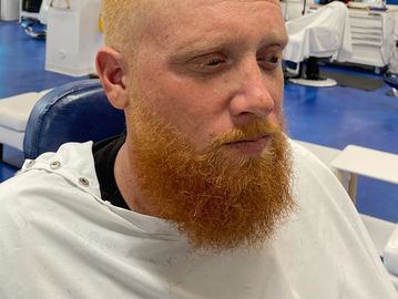 Man with a thick red beard sitting in a barber chair.