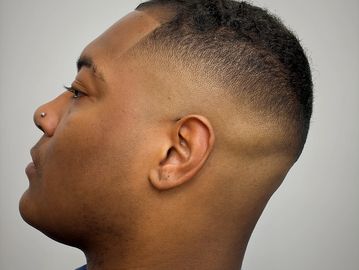 Side profile of a man with a fresh fade haircut and nose piercing.