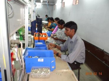 Workers assembling small components at a factory workstation.