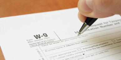 A person filling out a W-9 tax form with a pen.