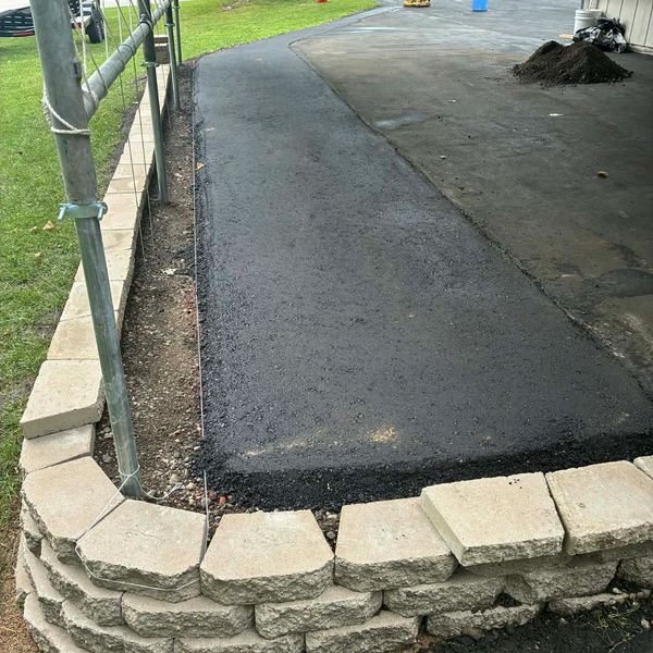 Newly paved asphalt path bordered by a stone retaining wall and metal fence.