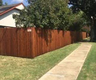 A wooden fence along a sidewalk beside a grassy lawn.