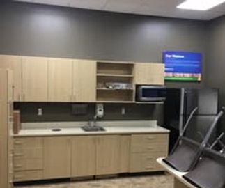 A clean office kitchen with wooden cabinets and a TV on the wall.