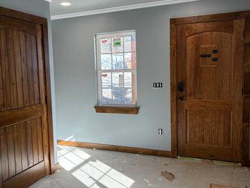 Sunlight casts window shadows on an unfinished room with wooden doors and gray walls.