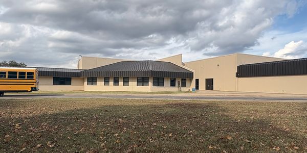 A school building with a yellow bus and a person pushing a trash bin.