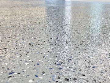 Close-up of a shiny speckled epoxy garage floor with organized shelves in background.