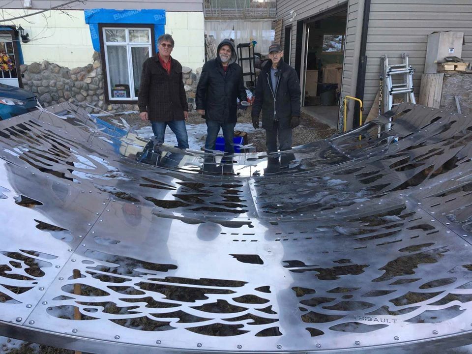 The three collaborators at the head of the  artwork, which is 100% stainless steel. The steel has been polished to a mirror-like finish to echo the theme  of
