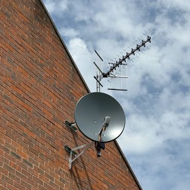Satellite dish and TV antenna mounted on a brick wall against a cloudy sky.
