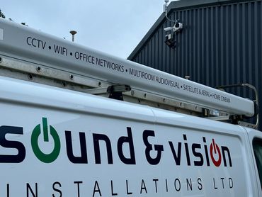 Service van for a sound and vision company parked outside with a security camera on the building.