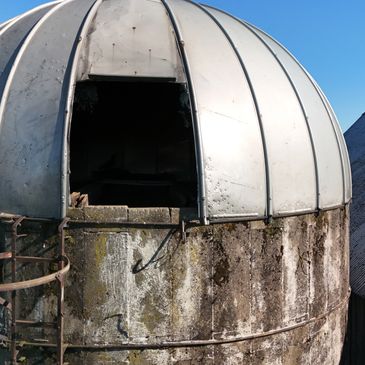 Old, weathered observatory dome with an open hatch under a clear blue sky.