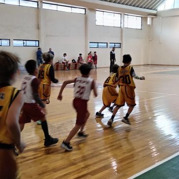 Kids playing basketball on an indoor court, wearing yellow and white jerseys.