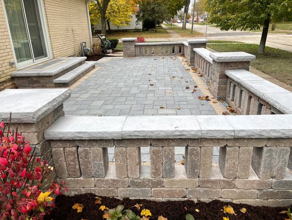 A stone patio with decorative railing and steps, surrounded by autumn foliage.