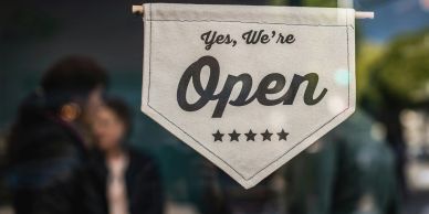 A sign on a glass door reads, "Yes, We're Open" with five stars below.