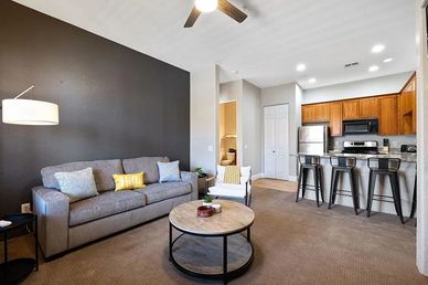 Modern living room with gray sofa and open kitchen with bar stools.