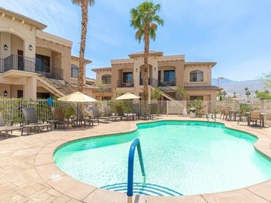 Sunny outdoor pool area with lounge chairs and umbrellas near residential buildings.