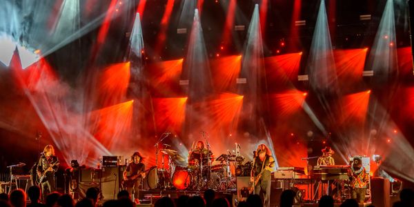 Rock band performing live with dramatic red and white stage lighting.