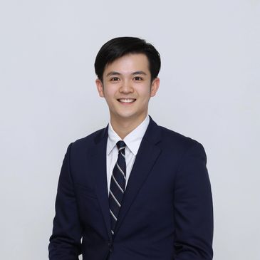 Young man in navy suit smiling against a plain background.