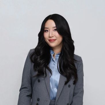 Confident woman with long black hair in a grey suit and blue shirt.
